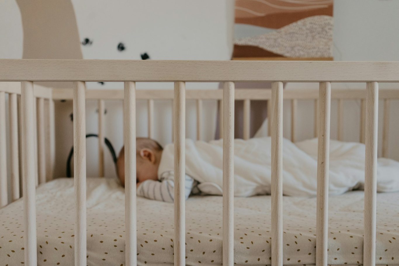 Sleeping baby in Cot A sleeping baby in a crib, wrapped in a blanket, with soft decor in the background.
