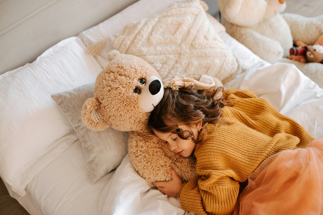 Toddler sleeping Child cuddling a large teddy bear on a cozy bed with soft pillows.